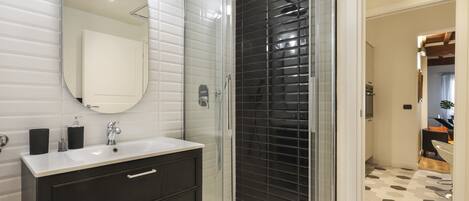 A modern bathroom with a glass-enclosed shower, a white sink with dark cabinets, and a large mirror.