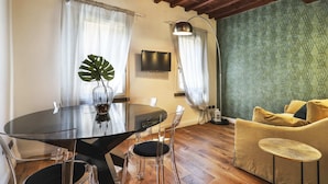Ein Essbereich mit Glastisch, Stühlen, einer Pflanze, einem Fernseher und einem Sofa.