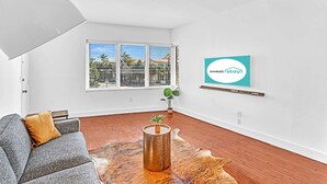 A modern living room with a grey sofa, a wooden coffee table, and a large window with blinds. - Garden Suite 3-hosted by Sweetstay (Miami Beach)