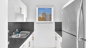A compact kitchen with white cabinets, a stainless steel refrigerator, and a window with a view of a building. - Garden Suite 3-hosted by Sweetstay (Miami Beach)