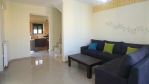 A living room with a dark-colored sofa, a coffee table, and a staircase leading to a kitchen. - Charming 4-bed House in Nikiana (Lefkada)