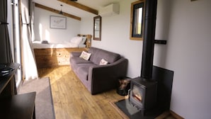 A cozy room with a sofa, a bed, a fireplace, and wooden beams on the ceiling. - 1 Bed Hut - Sleeps 4 - Pets - Parking (Minehead)