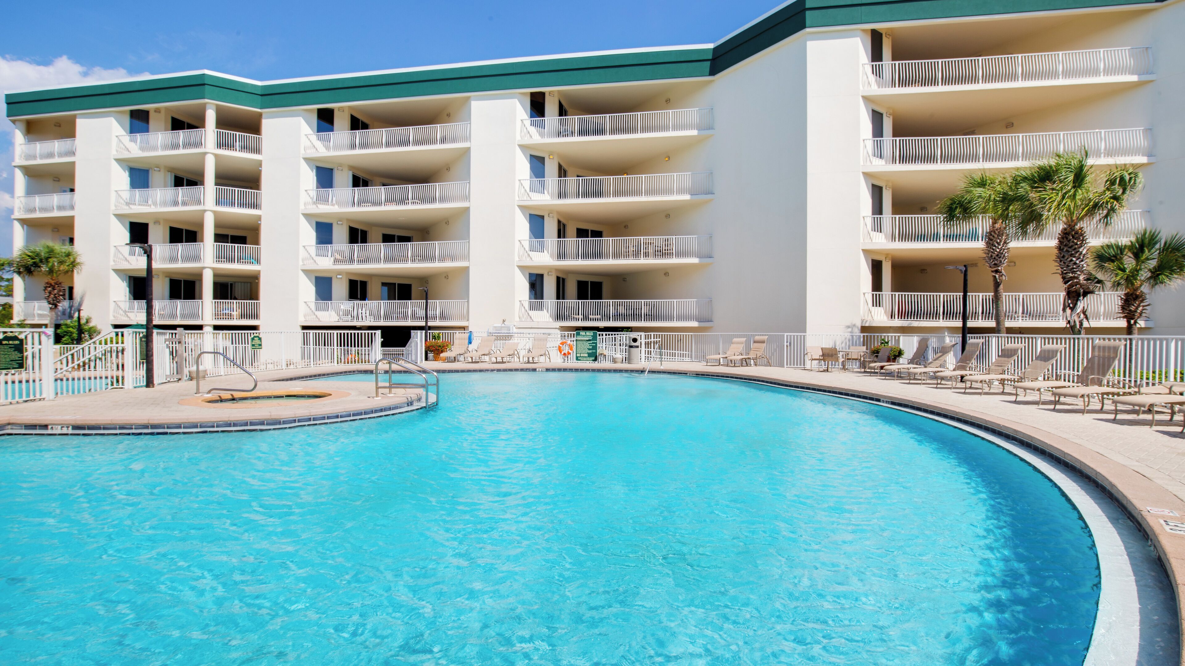 A hotel with a swimming pool, multiple balconies, and lounge chairs.
