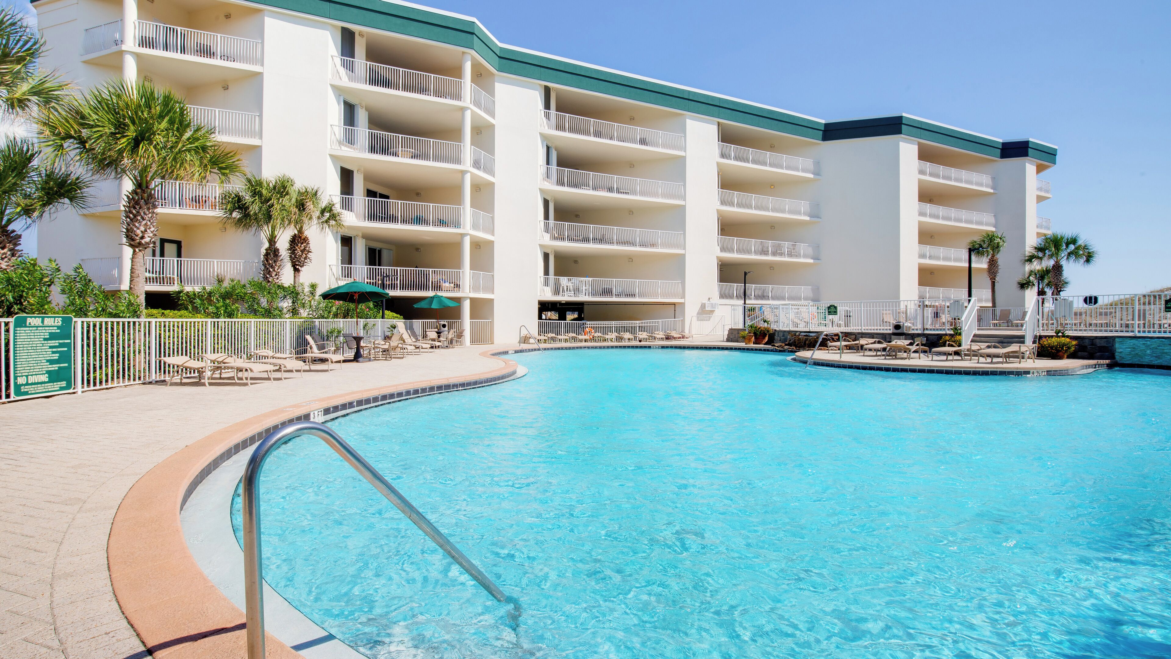 A hotel with a pool area, multiple balconies, and lounge chairs.