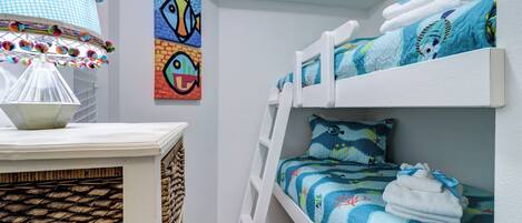 A bunk bed with a blue ocean-themed bedding, a white ladder, and a wall with colorful fish paintings.