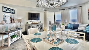 Un salon moderne comprenant un coin repas, un lustre, un téléviseur et une vue sur l’océan.