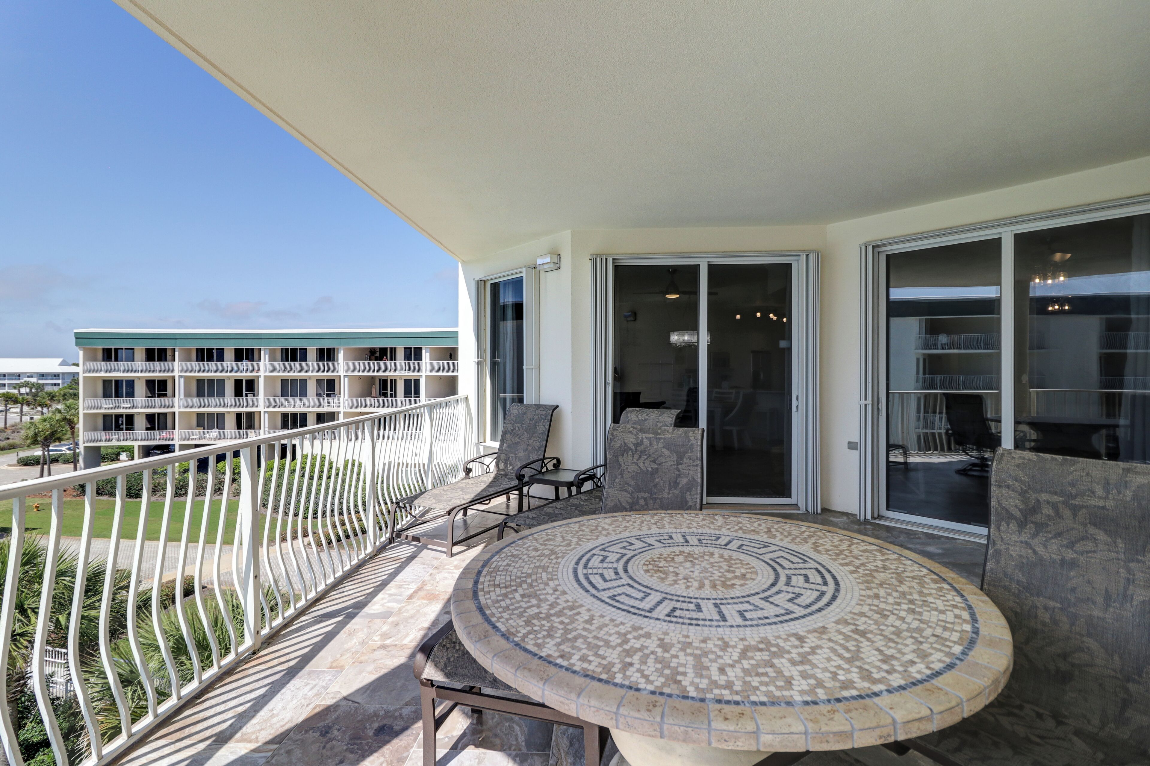 A balcony with a round table and chairs, a white railing, and a view of a building with multiple floors.