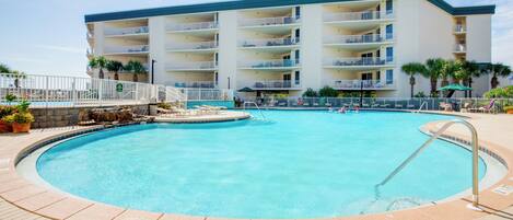 A hotel with a large swimming pool, multiple balconies, and a well-maintained outdoor area with palm trees.