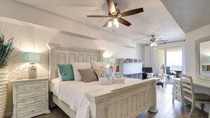 Une chambre avec un grand lit, un ventilateur de plafond et un bureau avec une chaise.