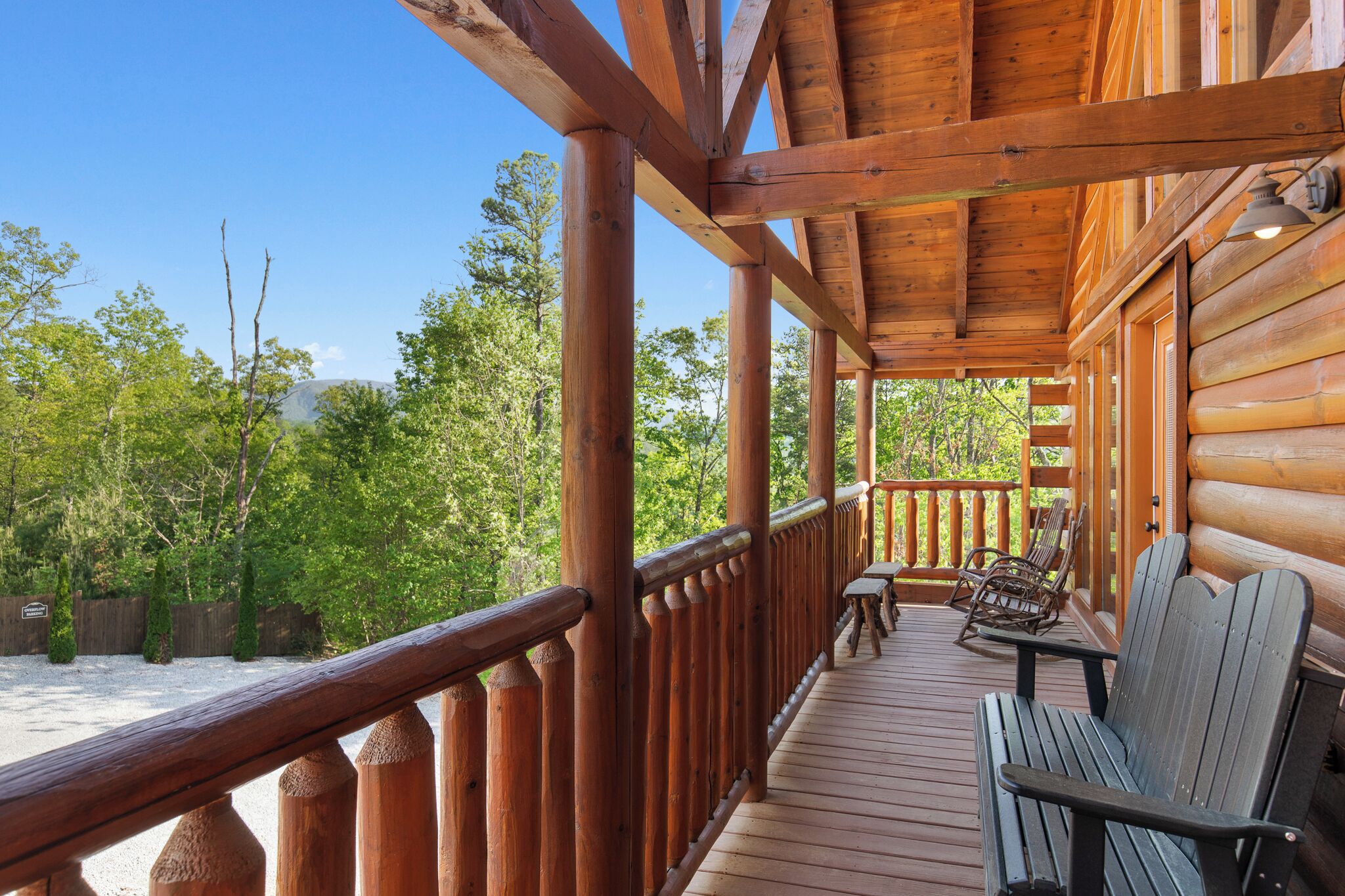 A wooden deck with a bench and chairs, surrounded by a wooden railing, overlooking a forested area.