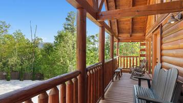 A wooden deck with a bench and chairs, surrounded by a wooden railing, overlooking a forested area.