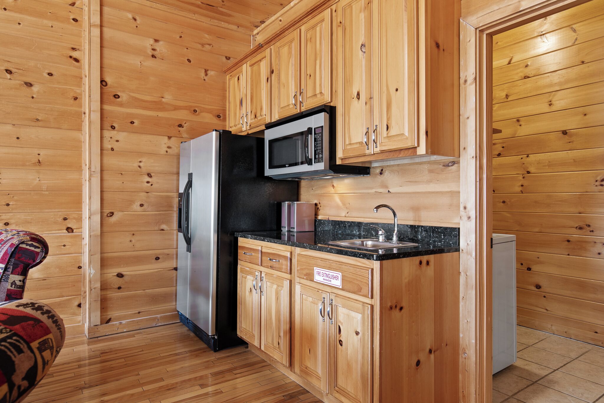 A compact kitchen with wooden cabinets, a refrigerator, a microwave, and a sink.