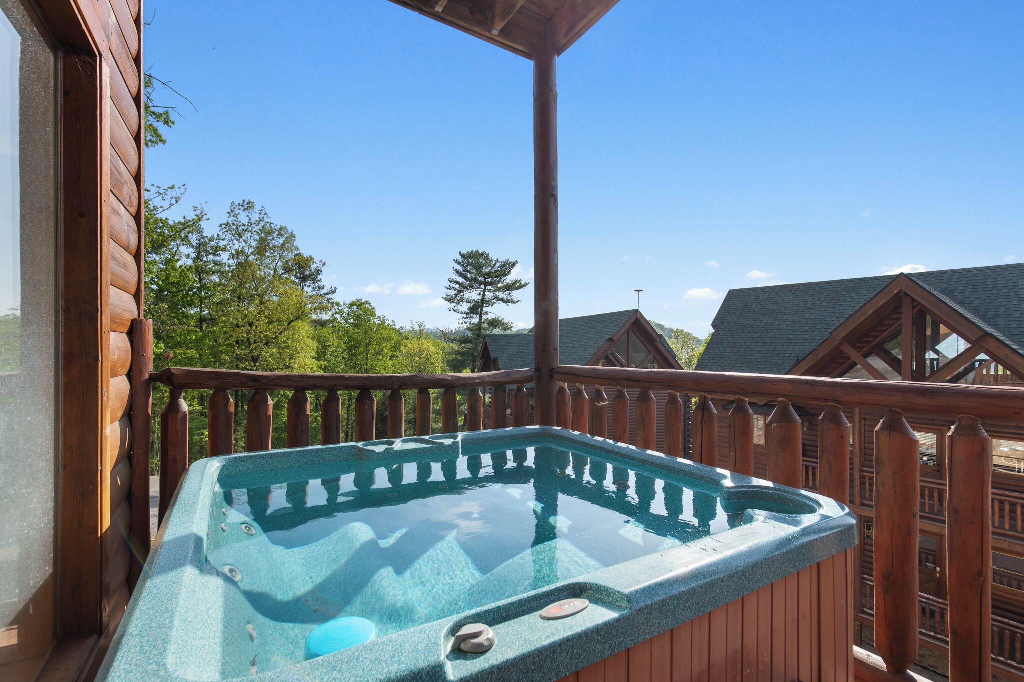 Ein Whirlpool auf einer Holzterrasse mit Blick auf umliegende Blockhütten.