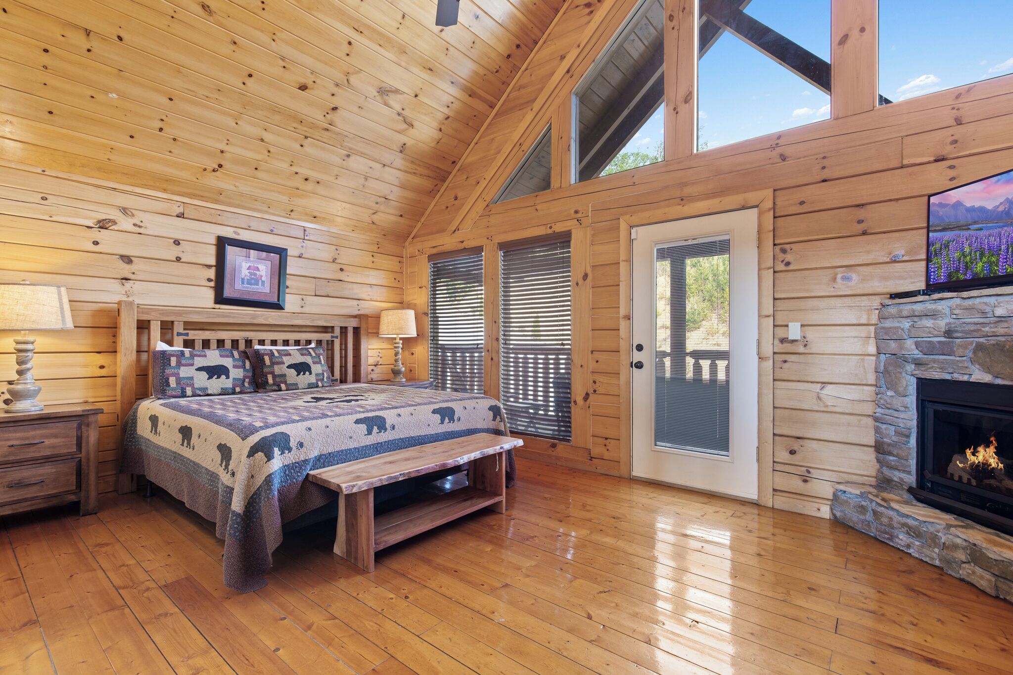 A wooden cabin bedroom with a bed, bedside table, lamp, and a stone fireplace.