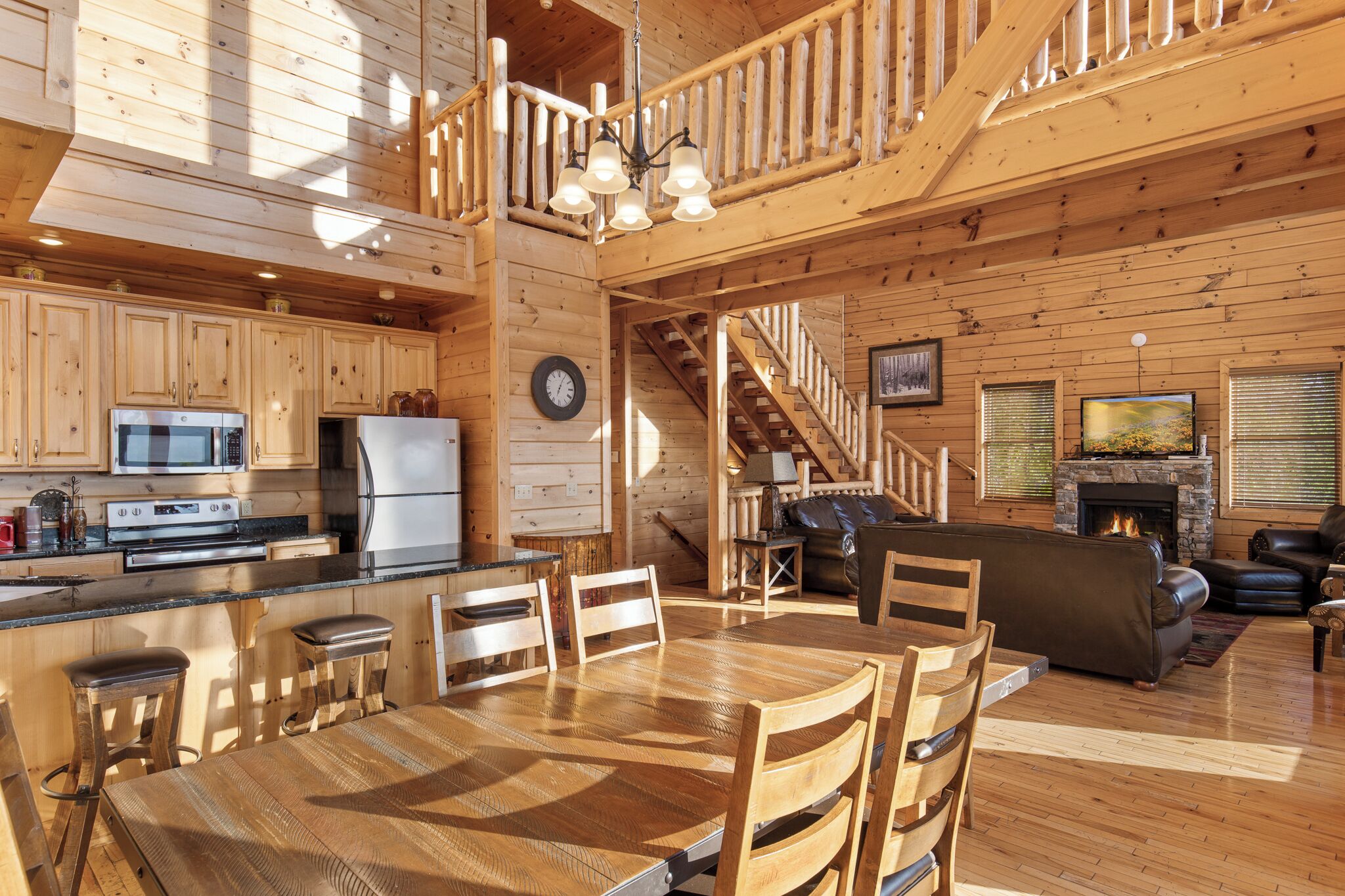 Ein großzügiges Blockhaus-Interieur mit Küche, Essbereich und Wohnzimmer, mit Holzböden, einem Kamin und einer Treppe.
