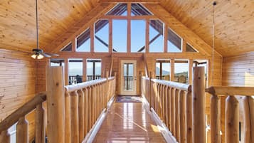 A wooden interior with a high ceiling, large windows, and a central door leading to an outdoor area.