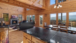 A spacious wooden cabin with a fireplace, a dining area, and large windows offering mountain views. - Theatre in the Mountains by Jackson Mountain Rentals (Sevierville)
