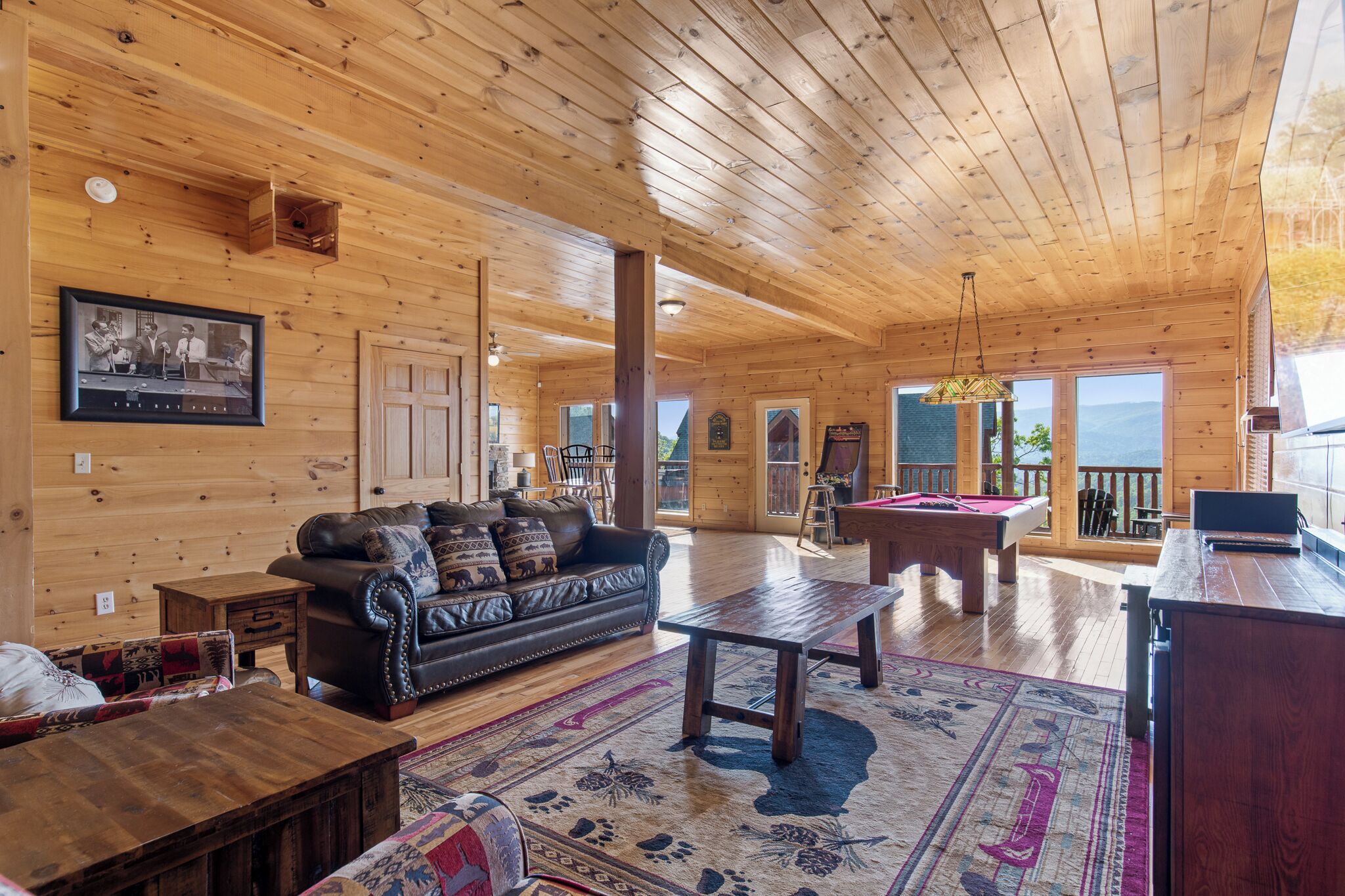 A spacious wooden cabin interior with a living area featuring a sofa, coffee table, and pool table.