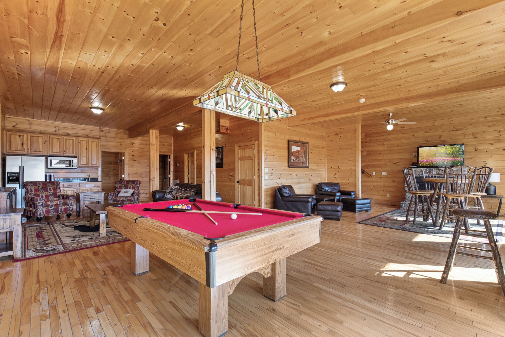 A wooden cabin interior with a pool table, dining area, and kitchen.