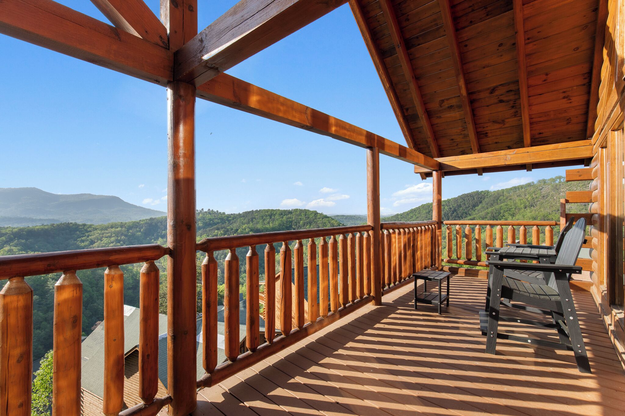 A wooden deck with a view of mountains, a table, and a chair.