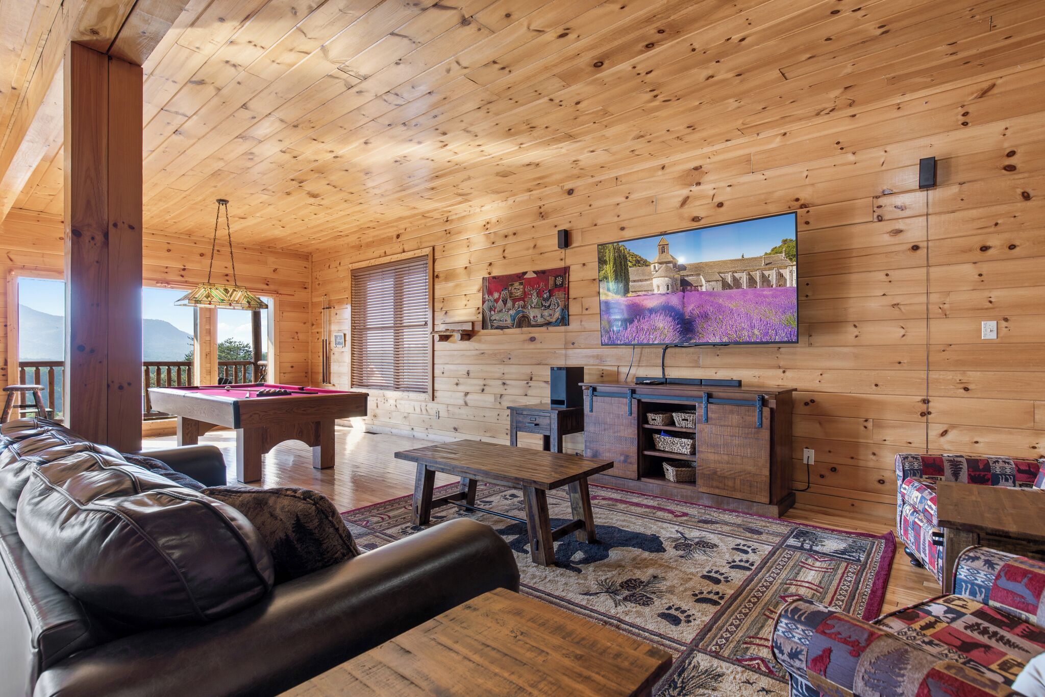 L’intérieur d’un chalet en bois est aménagé avec une table de billard, un canapé en cuir et un téléviseur fixé au mur.