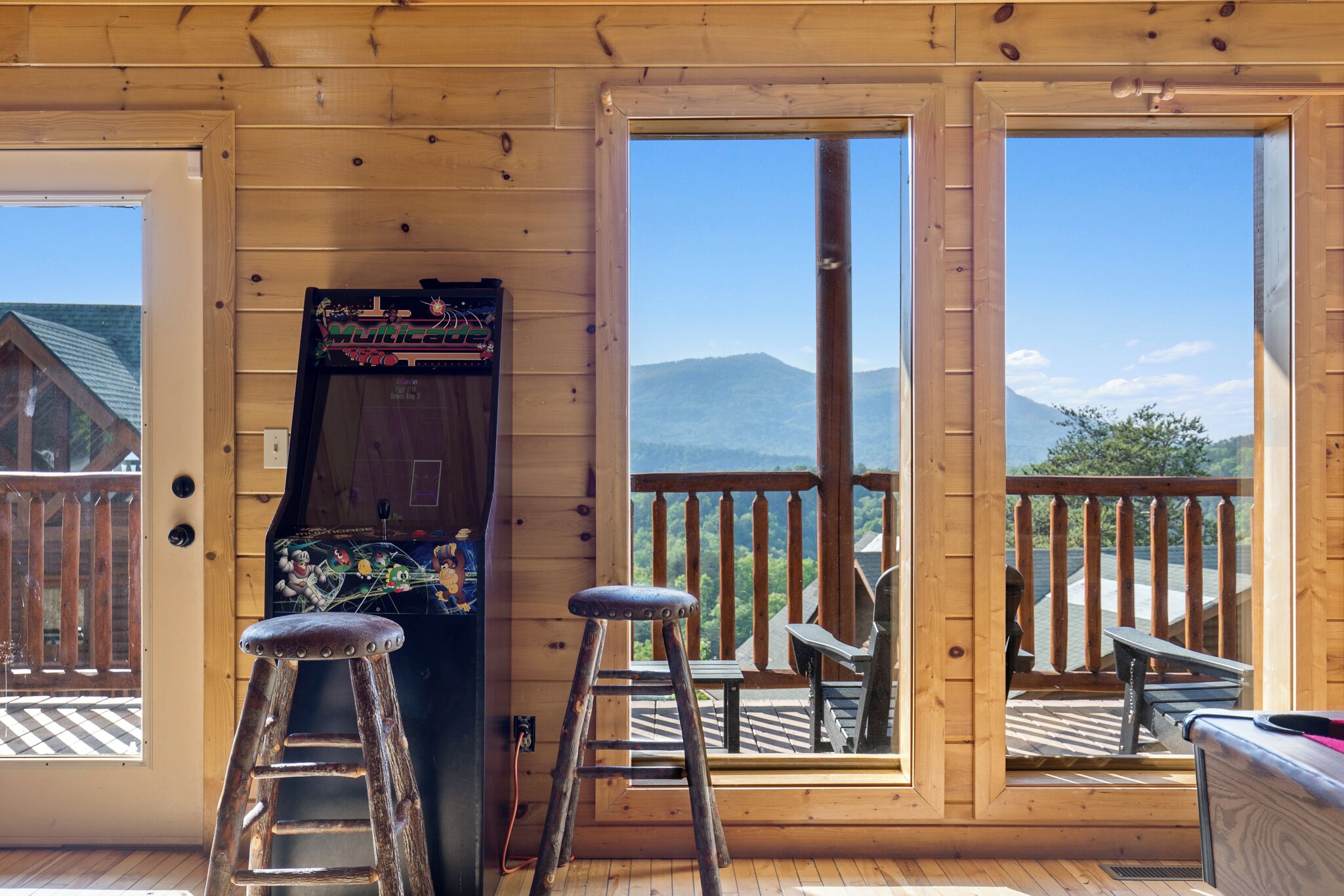 Una cabaña de madera con balcón, puerta de madera y una máquina recreativa antigua.