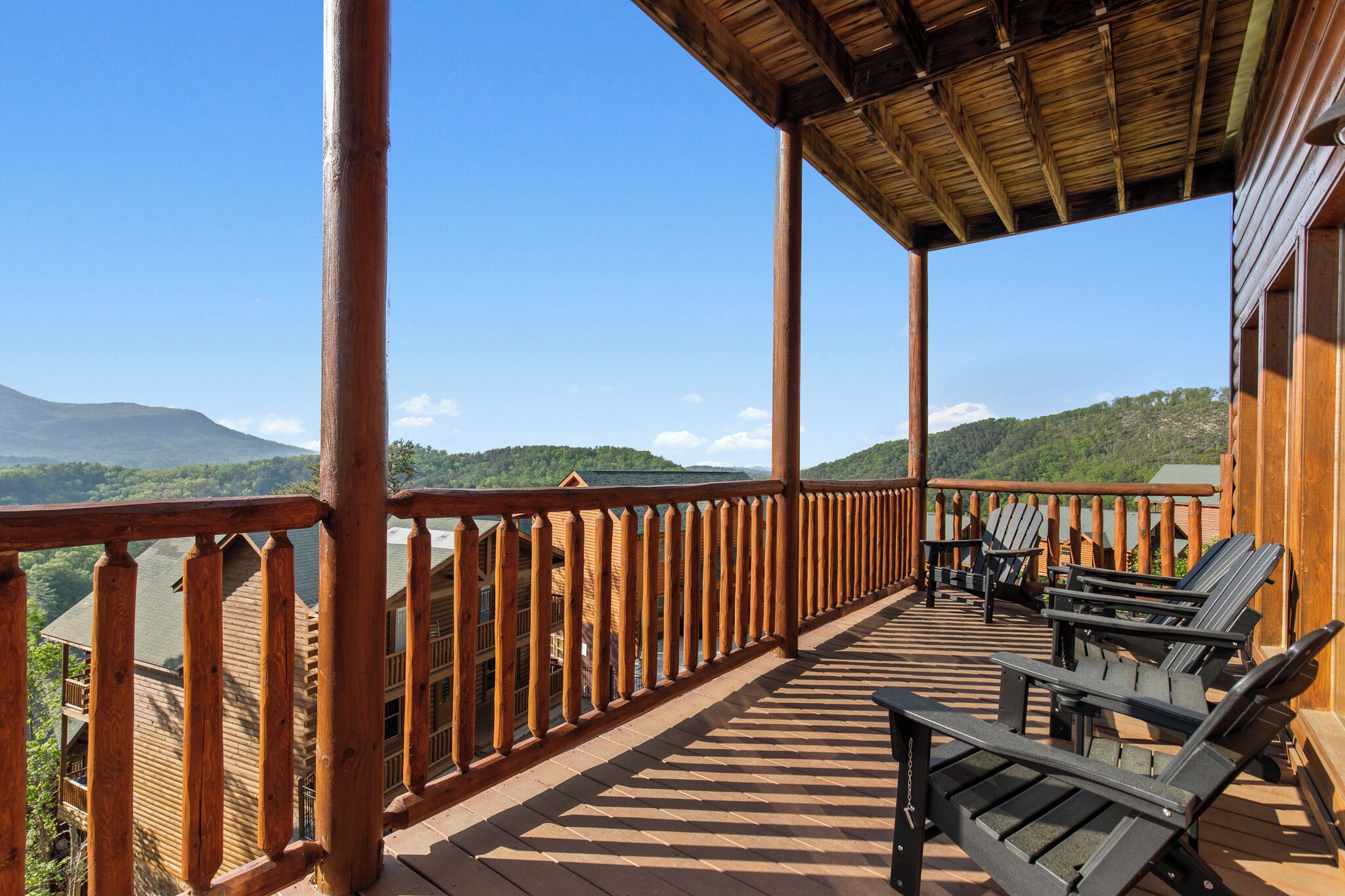 Eine Holzterrasse mit Holzgeländer, Sitzgelegenheiten im Freien und Blick auf eine Berglandschaft.