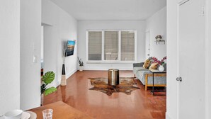 Un salon moderne avec un plancher en bois, un tapis en peau de vache, un canapé avec des coussins, une table basse et un tableau accroché au mur.