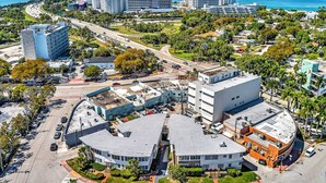 Vue aérienne d’une zone commerciale avec un bâtiment rond, des parkings et un paysage côtier en arrière-plan.