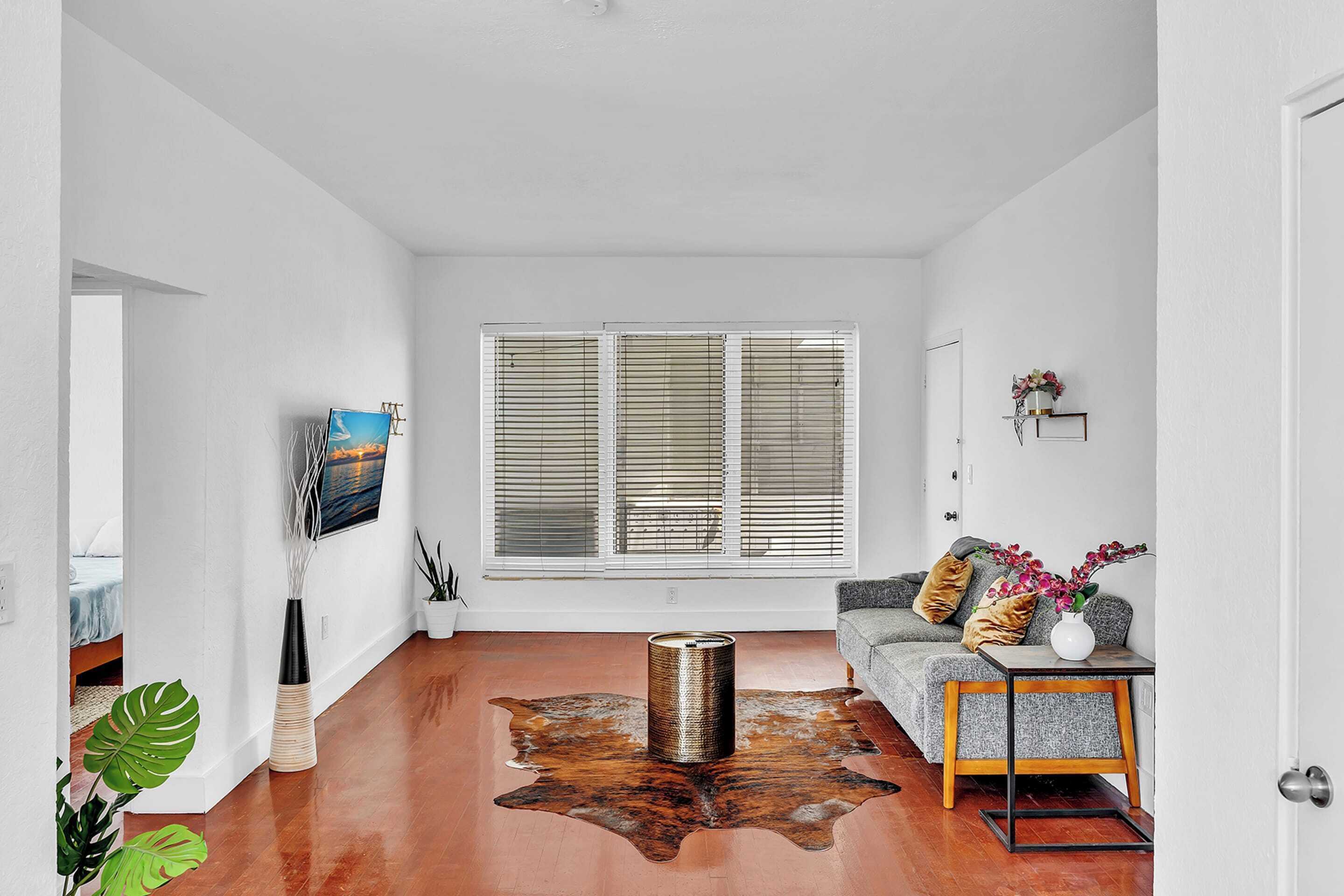 A modern living room with a large window, a sofa, a coffee table, and a unique cowhide rug.