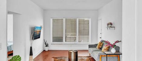 A modern living room with a large window, a sofa, a coffee table, and a unique cowhide rug.