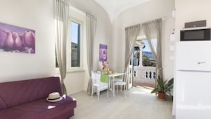 Una sala de estar con un sofá morado, una mesa de comedor con sillas, un refrigerador y vistas al exterior.