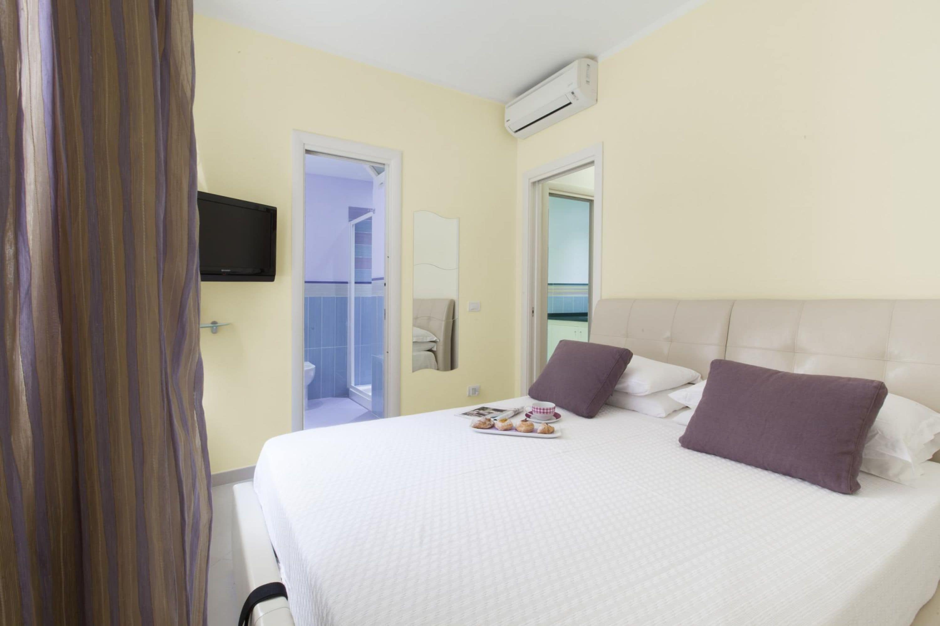 Ein Hotelzimmer mit Bett, Flachbildfernseher, Klimaanlage und einem durch eine geöffnete Tür einsehbaren Badezimmer.