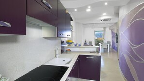 Una cucina moderna con piano cottura nero, lavandino bianco e mobili viola. Si vede una finestra con vista sull'esterno.