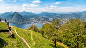 A scenic view of a mountainous landscape with a lake, a town in the valley, and a path leading to a viewing platform.