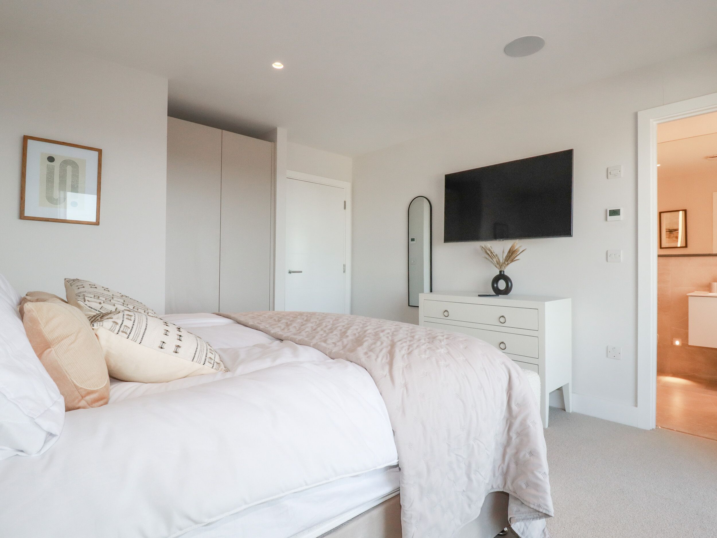 Une chambre à coucher avec un lit, une commode, un miroir et un téléviseur fixé au mur.