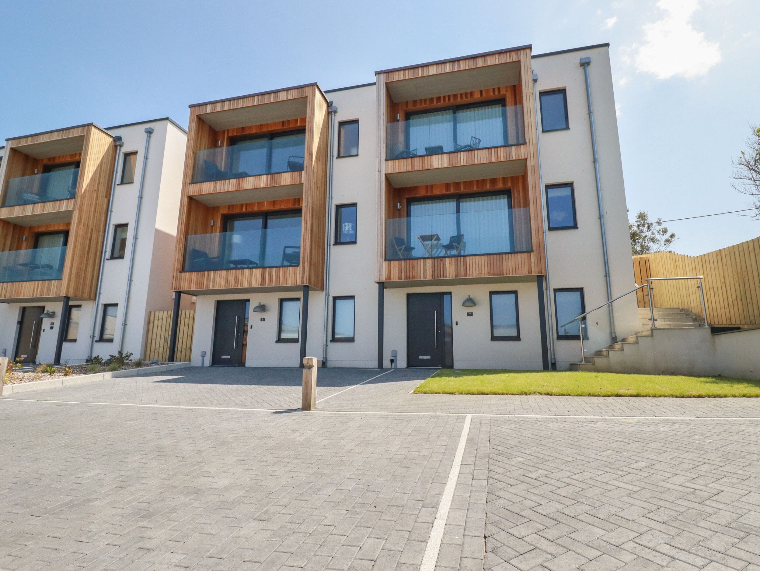 A modern apartment building with multiple balconies, large windows, and a paved entrance area.