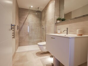 Et moderne badeværelse med en brusekabine i glas, toilet og et spejl med vaskebord.