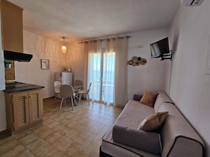 A living area with a sofa, a dining table with chairs, a kitchenette, and a TV mounted on the wall. - Corfu Dream Glyfada Apartments (Corfu)