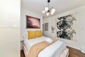 A modern bedroom with a large bed, a ceiling light fixture, and two abstract paintings on the walls.