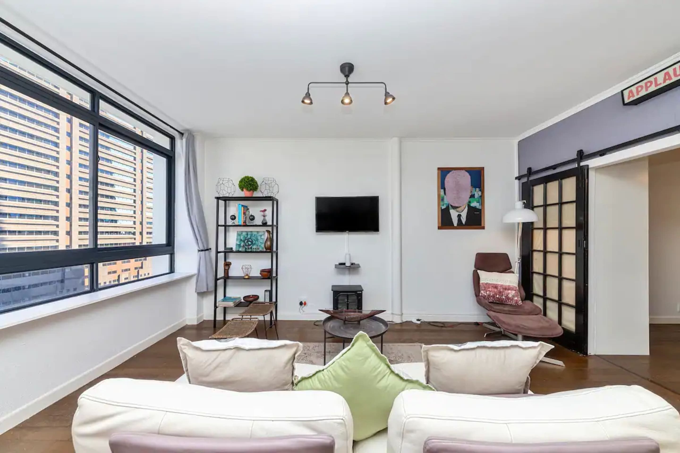 A modern living room with a sofa set, a TV, a bookshelf, and a view of a cityscape through large windows.