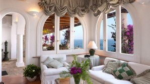 A cozy room with white furniture, large windows with curtains, and a view of the sea. - Villa San Montano in Massa Lubrense (Massa Lubrense)