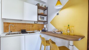 A modern kitchen with white cabinets, a microwave, a sink, and a wooden countertop. There are two yellow chairs and a yellow pendant light. - Casa Cristina Yellow (Sorrento)