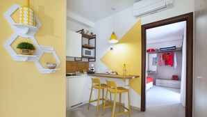 A modern kitchen with white cabinets, a microwave, and a yellow accent wall. There are two wooden stools and a pendant light. - Casa Cristina Yellow (Sorrento)