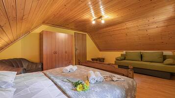 A cozy room with a sloped ceiling, wooden furniture, a bed with rolled towels and a book, a green sofa, and a wooden wardrobe.