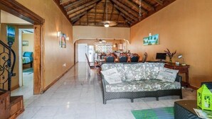 A spacious living area with a high wooden ceiling, a sofa with floral cushions, a dining table with chairs, and a kitchen in the background. - Yanceylargo Estate - Newly Renovated 7br Beautiful Two-story Estate Villa W Gorgeous Mountain View 7 Bedroom Villa by RedAwning (Montego Bay)