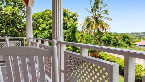 A balcony with white railings and a view of lush greenery and palm trees. - Yanceylargo Estate - Newly Renovated 7br Beautiful Two-story Estate Villa W Gorgeous Mountain View 7 Bedroom Villa by RedAwning (Montego Bay)