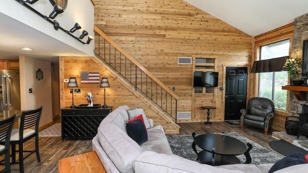 Un salon spacieux avec un plafond en bois, un escalier, une cheminée et un téléviseur.