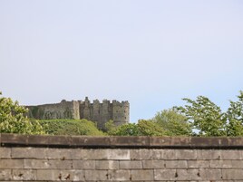 A historic stone castle with multiple towers and crenellations, surrounded by greenery and a low stone wall in the foreground.