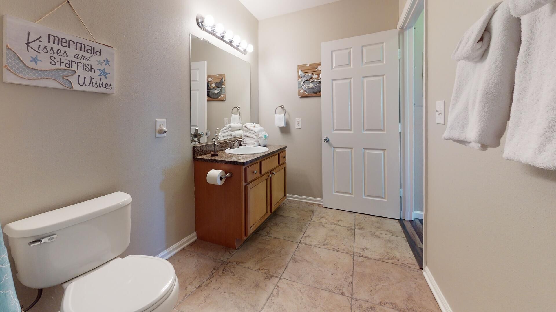 Une salle de bain avec des toilettes, un lavabo et un meuble-lavabo. Il y a un panneau sur le mur et une porte sur laquelle est accrochée une serviette.